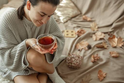 attractive-young-woman-is-drinking-tea-sitting-bed-among-autumn-leaves drinking black tea